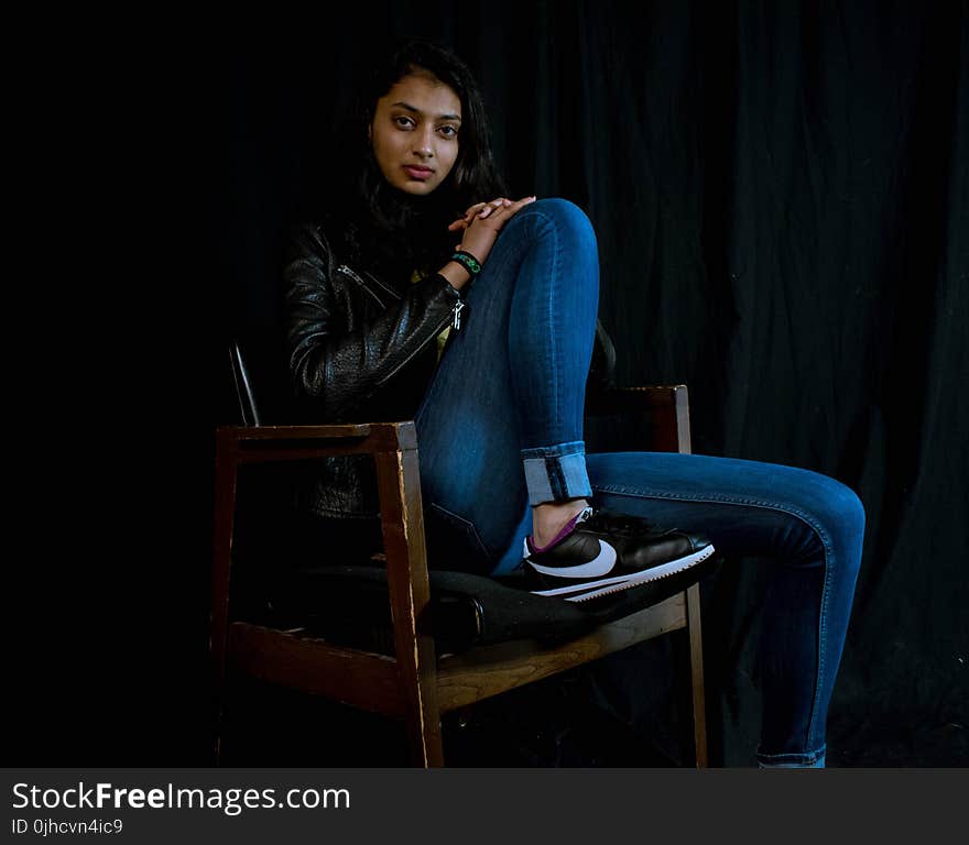 Woman Wearing Blue Jeans Sitting on Brown Wooden Armchair