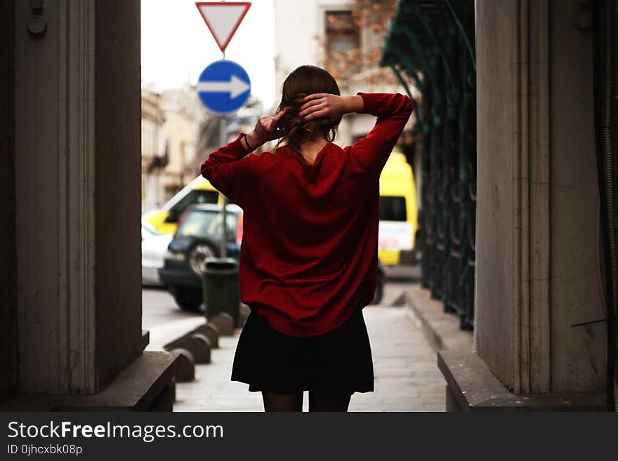 Woman in Red Sweater and Black Miniskirt Holding Hair Facing Road