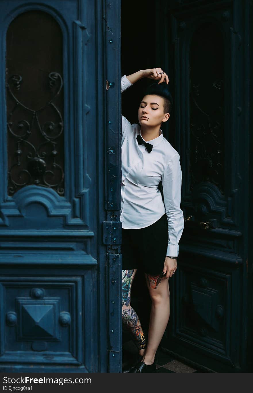 Woman in White Dress Shirt With Bow-tie Leaning on Blue Wooden Door