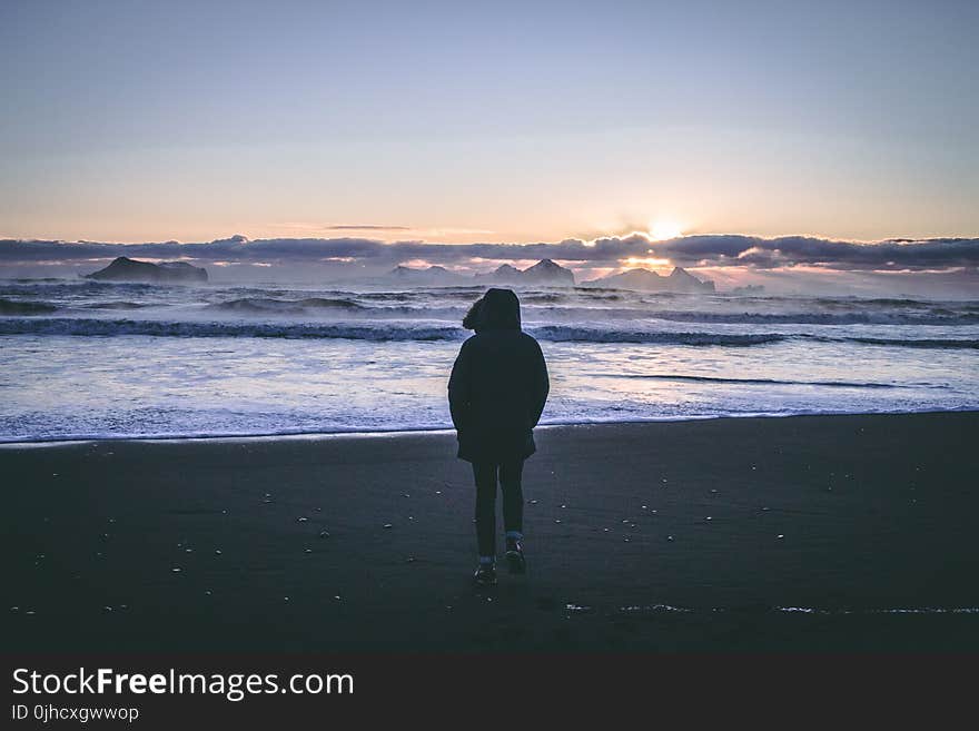 Person in Black Hoodie Near Seashore during Sunset