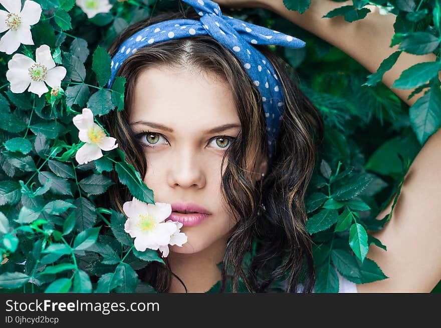 Portrait Photo of Woman in White Top and Blue Polka Dot Headband Near Flowers