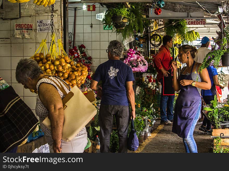 Photo of People Standing on Grey Concrete Surface Surrounded With Plants and Vegetables