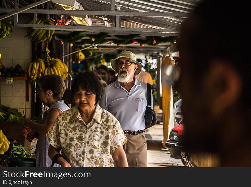 Man in Purple Polo Shirt and Brown Hat Behind Woman in Brown and White Floral Button-up T-shirt