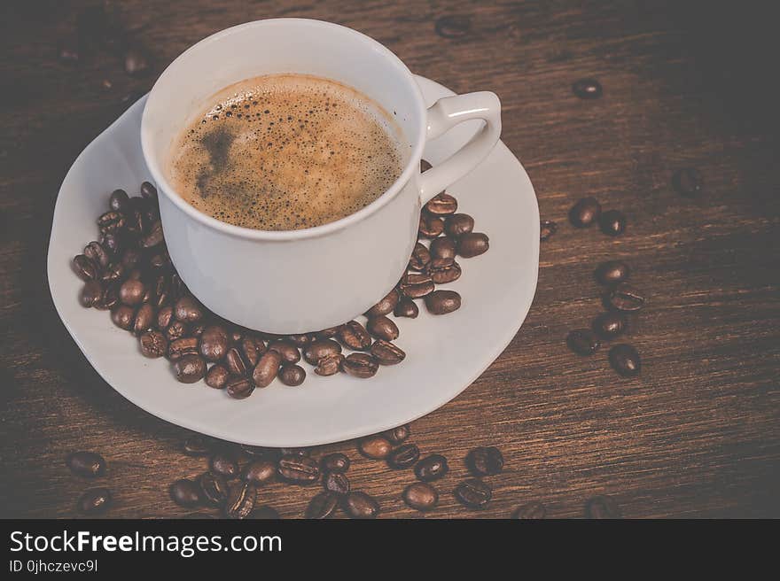 A Cup of Coffee on Brown Wooden Table With Coffee Seeds