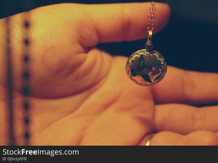 Person Holding Round Silver-colored Necklace Pendant