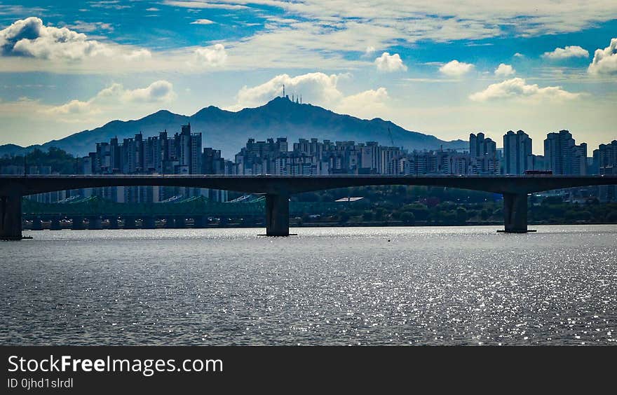 Grey Concrete Bridge Near Cities and Mountain at Daytime