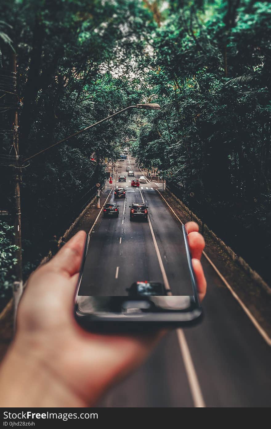 Forced Perspective Photography of Cars Running on Road Below Smartphone