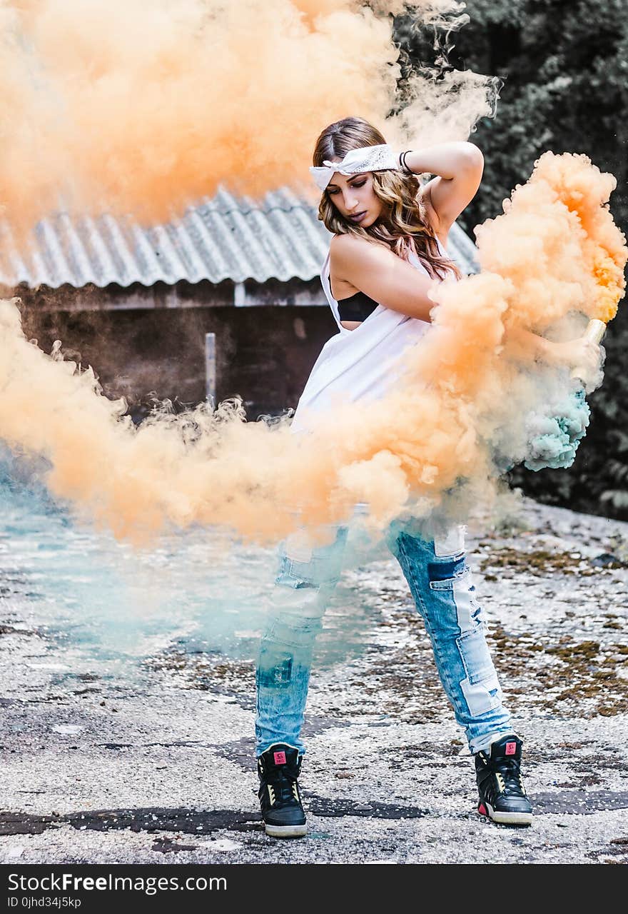 Woman Wearing White Tank Top and Blue Jeans Surrounded by Orange and Blue Smokes