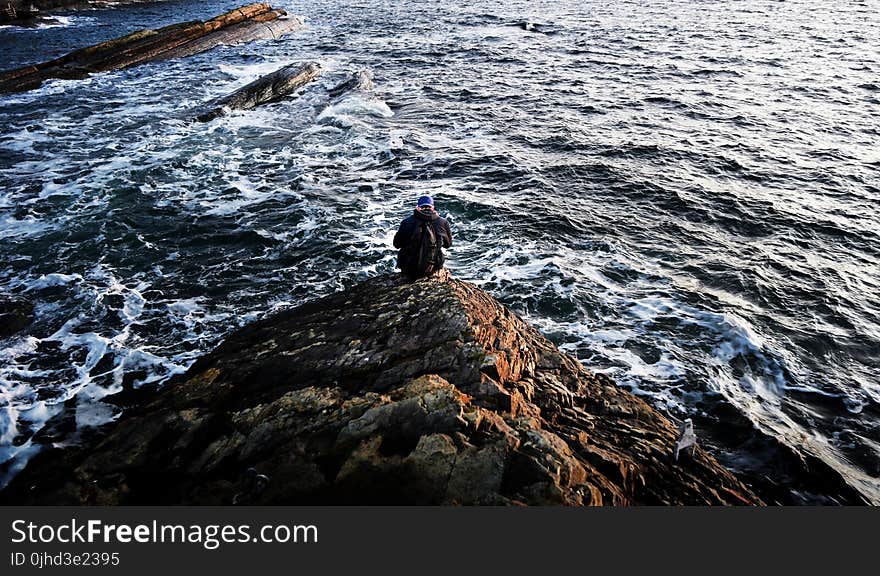 Photography of Person Sitting on Rock Near Ocean