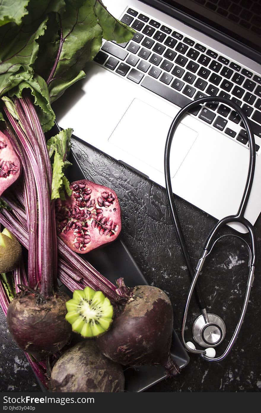 Macbook Pro With Stethoscope With Kiwi and Vegetables on Black Wooden Surface