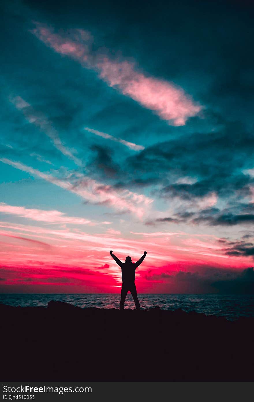 Silhouette of Man Raising Hands Against a Red Sunset Light Under Green Clouds