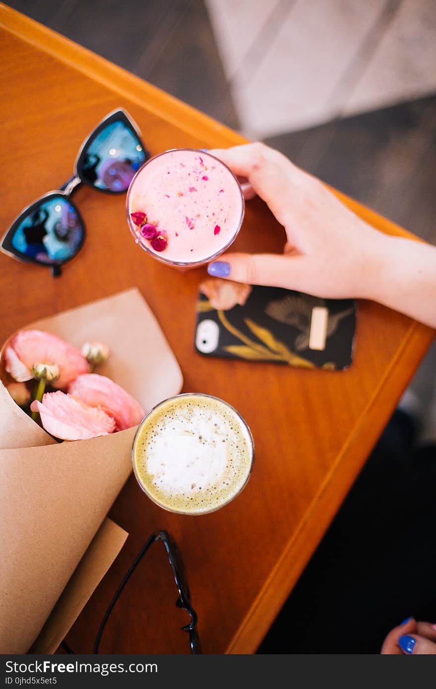 Woman Holding Beverage Filled Cup Near Sunglasses and Phone