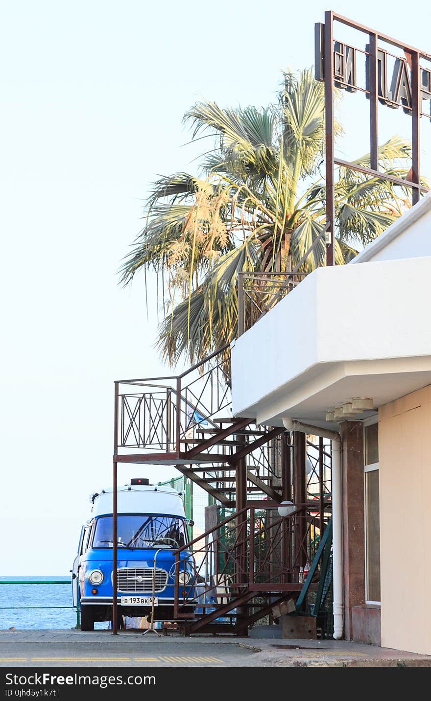 Blue Vehicle Park Near Brown Metal Outdoor Stairs and White Concrete House at Daytime