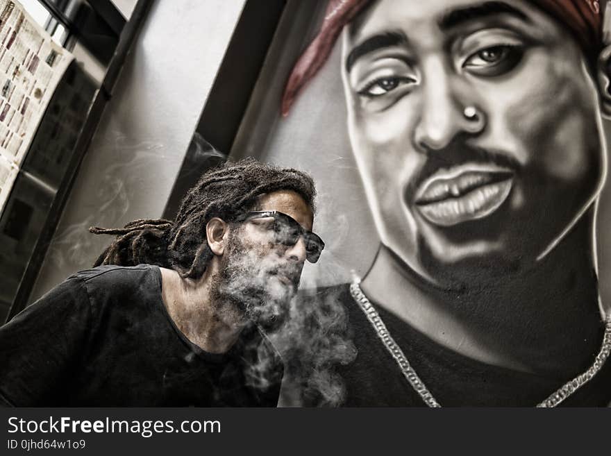 Man With Dreadlocks and Sunglasses Poses Near Tupac Shakur Portrait