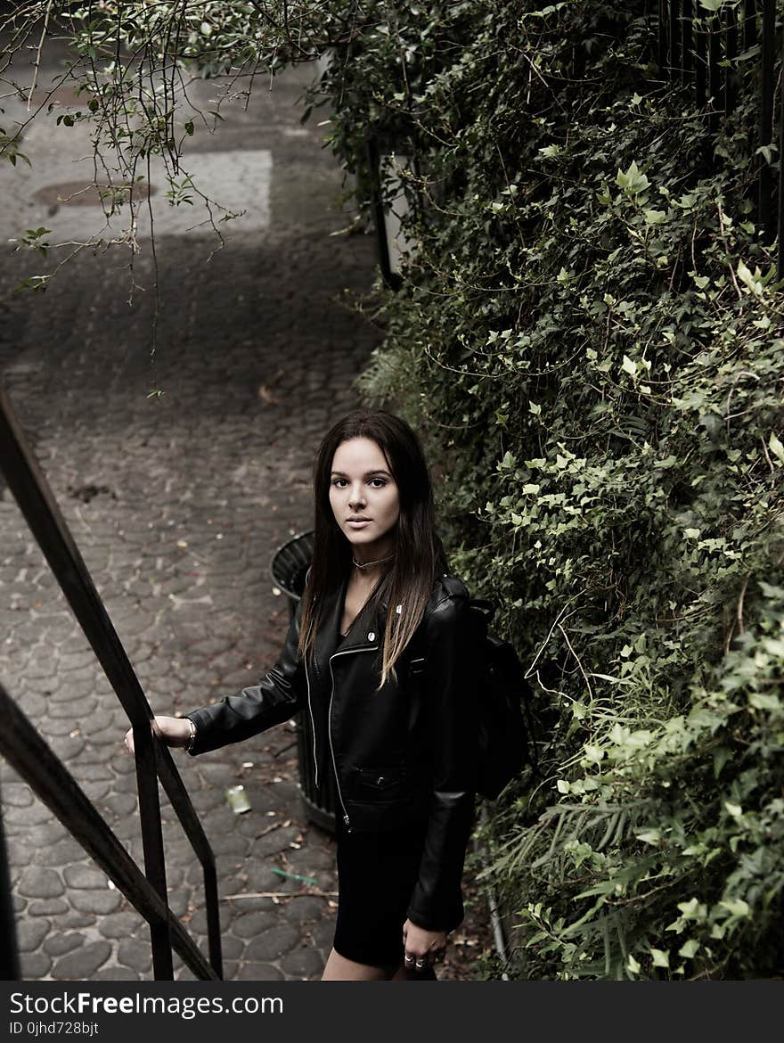 Close Up Photograph of Woman With Black Leather Jacket Standing Beside Stair Handle