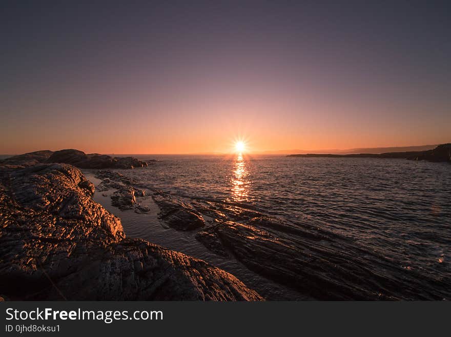 Brown Rocks Beside Body of Water during Sunset