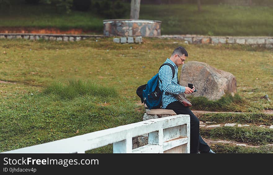 Man Sitting on White Railing Near Rock