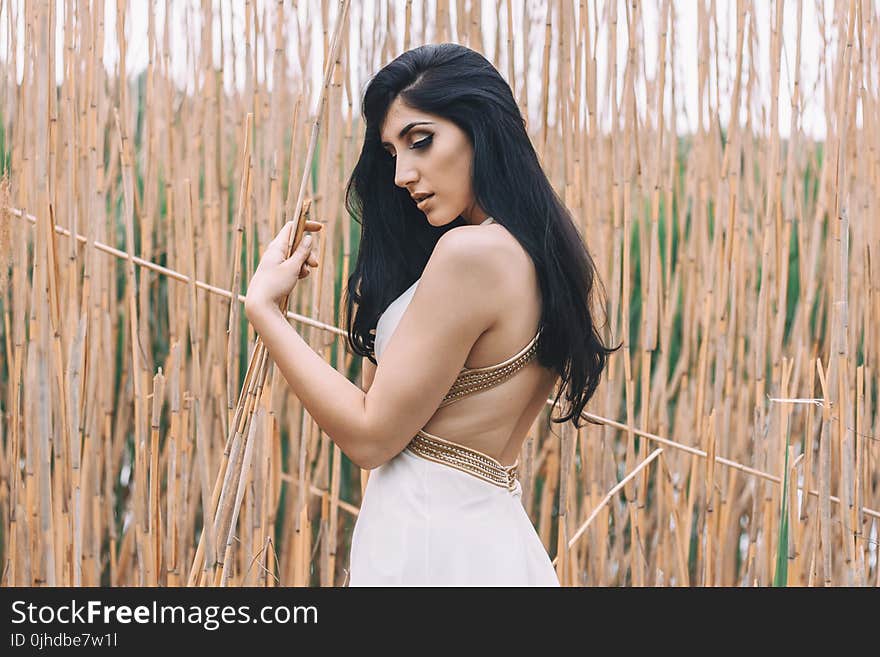 Woman in White Backless Dress in Front of Bamboo Sticks