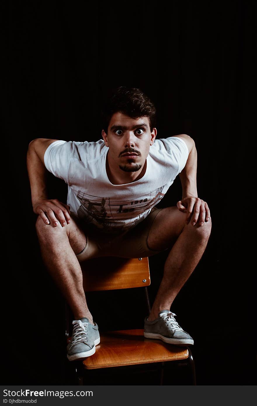 Man Wearing White Crew-neck Short-sleeved Shirt Sitting on Brown Wooden Chair