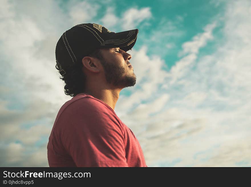 Man Wearing Black Cap With Eyes Closed Under Cloudy Sky