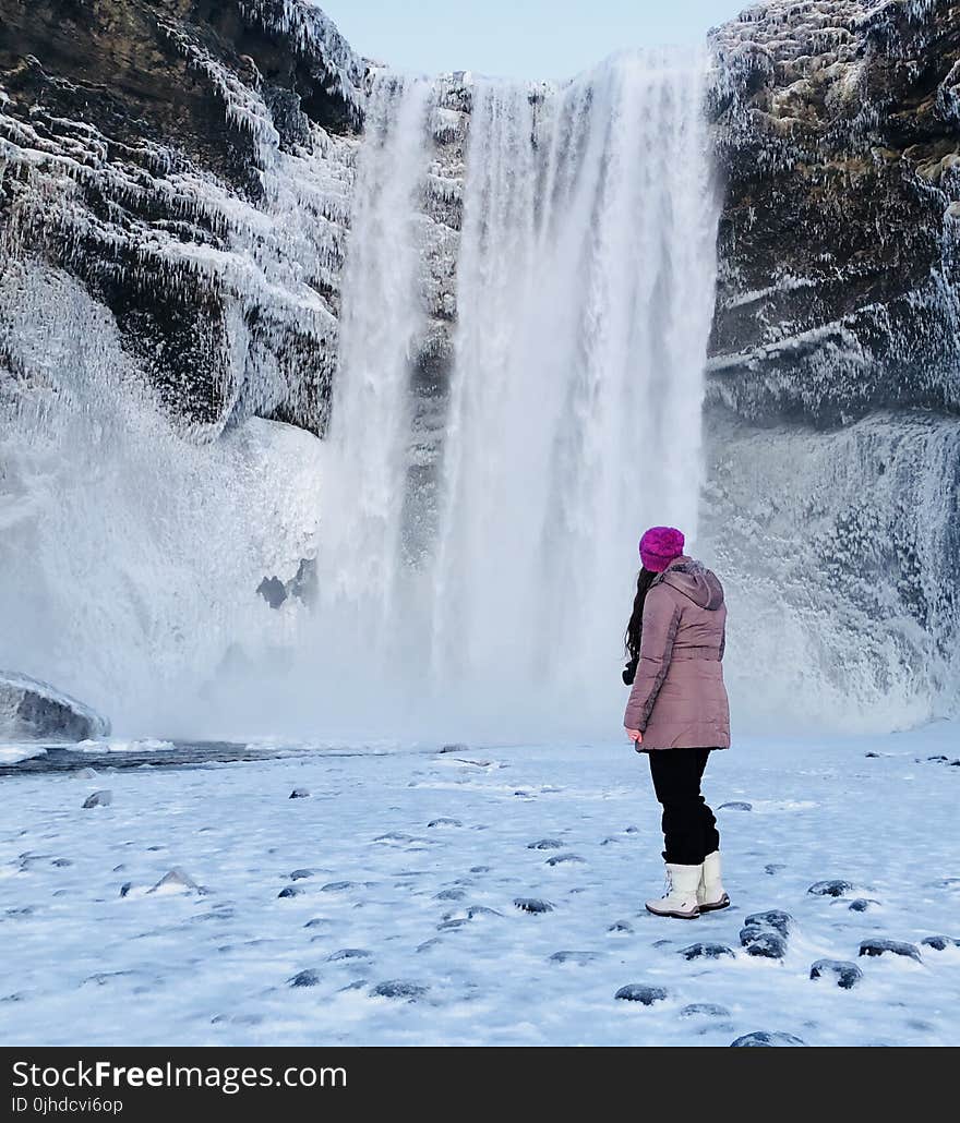 Woman Wearing Pink Snow Coat Standing on Field Full of Snow in Front of Frozen Waterfalls
