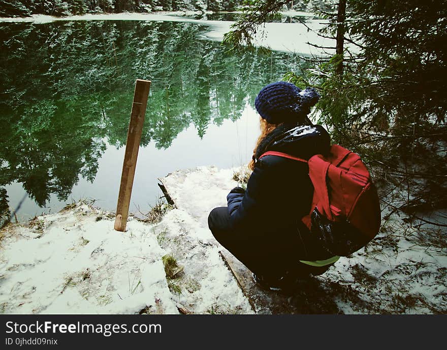 Girl Wearing Black Jacket Sitting In Front Of Calm Body Of Water