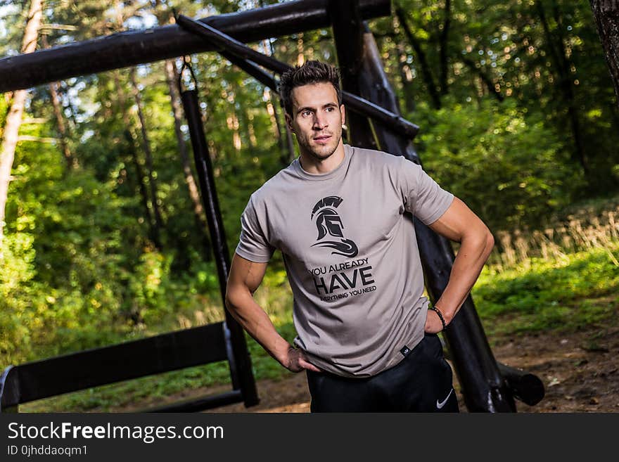 Man Wearing Brown Crew-neck T-shirt Standing Near Brown Wooden Swing at Daytime