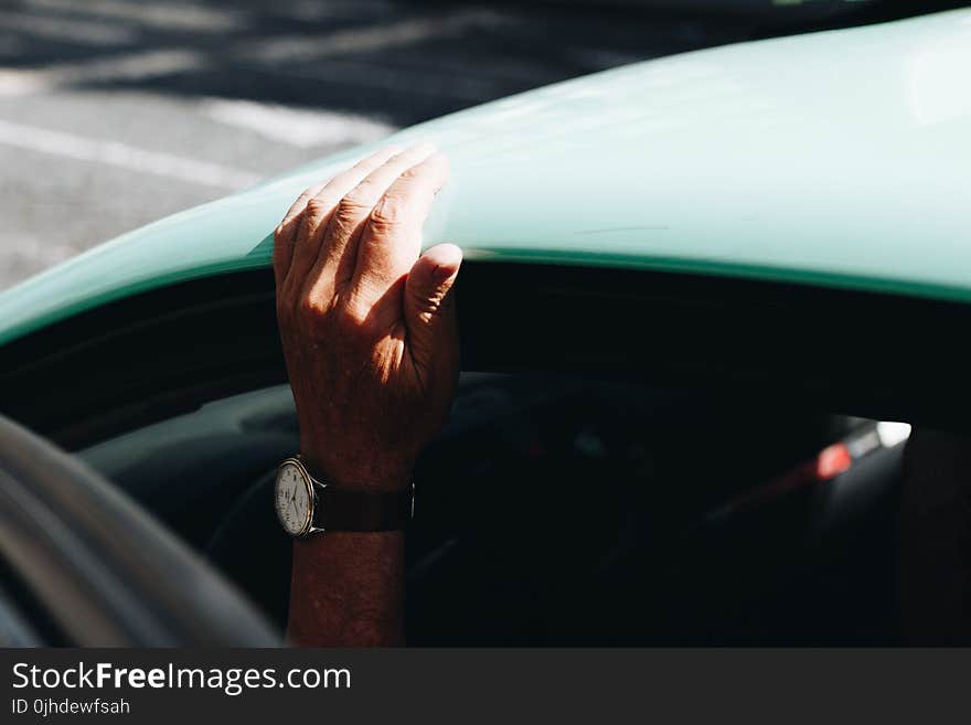 Person Wearing Round White Analog Watch Black Strap Holding on Vehicle Roof