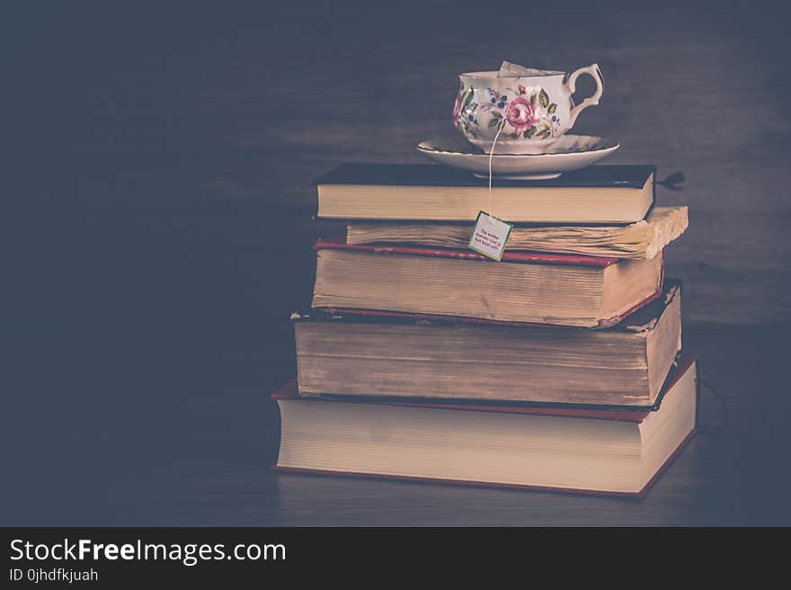 Pile of Hardbound Books With White and Pink Floral Ceramic Teacup and Saucer