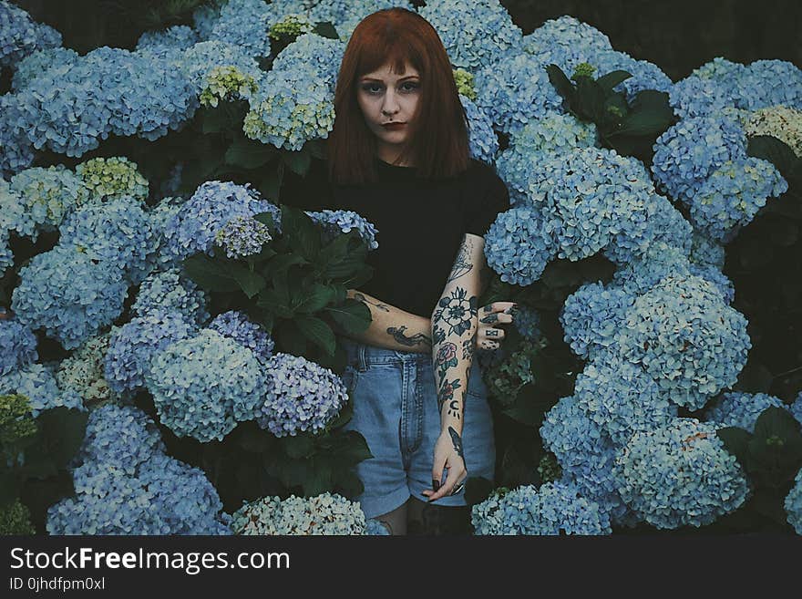 Woman With Black and Red Flower Tattoo Standing Behind Blue Flowers