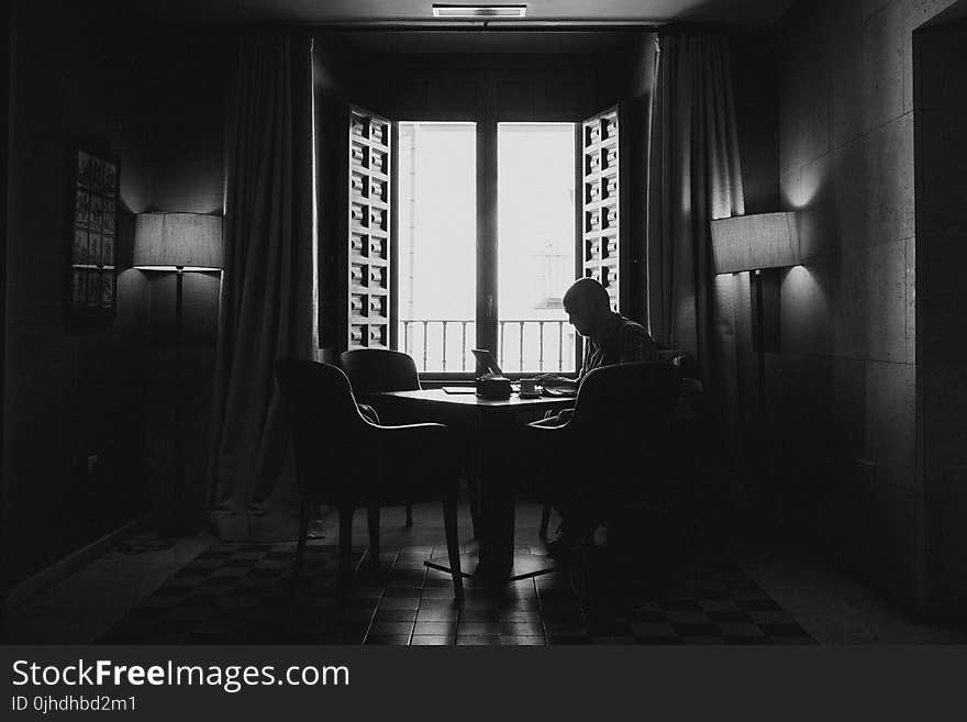 Silhouette Photography Of Man Sitting On Chair Beside Open Window