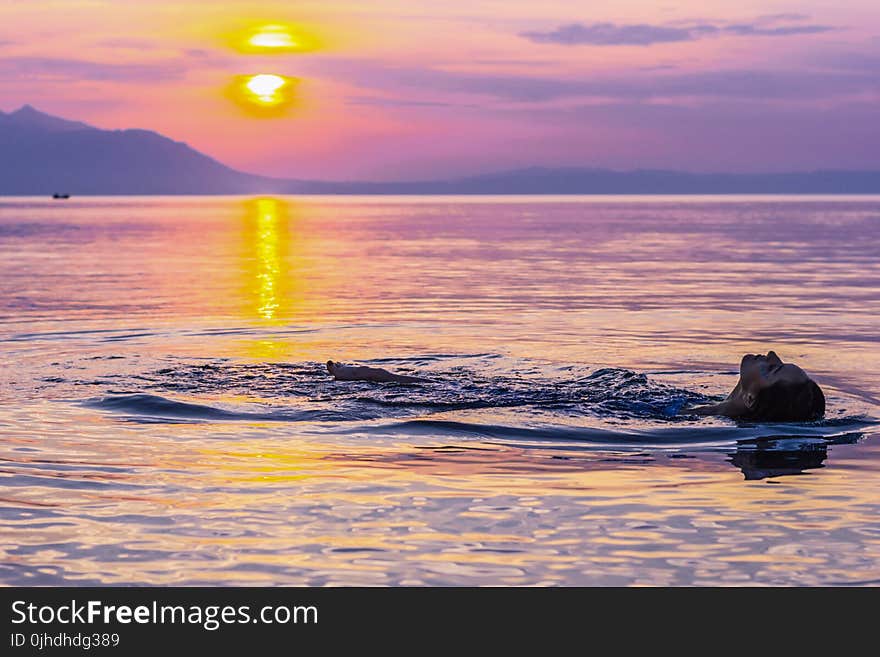 Person Swimming on Body of Water during Golden Hour