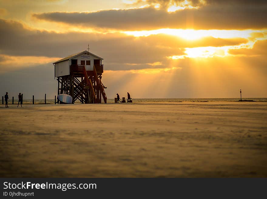 White Lifeguard House on Beach Taken Under White Clouds and Orange Sky