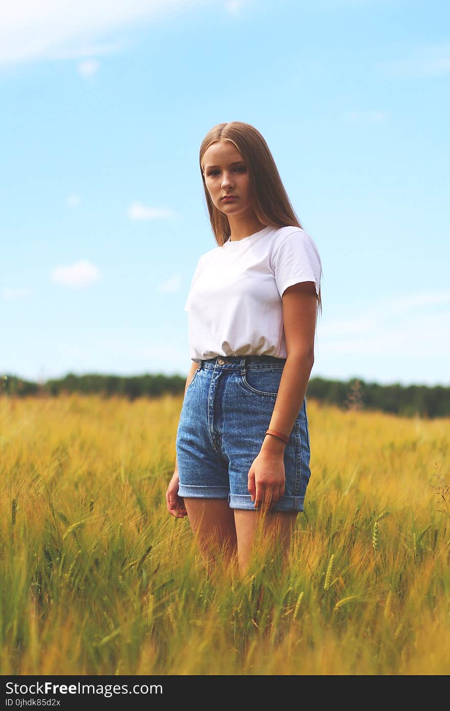 Woman Wearing White Crew-neck T-shirt, Blue Denim Cuff Short Shorts While Standing on Grass Field