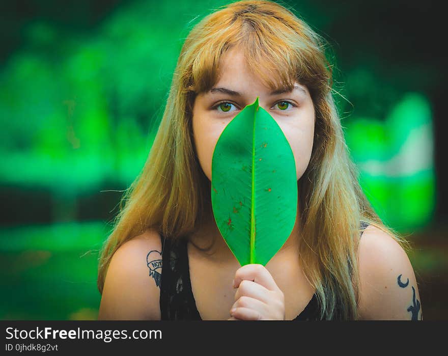 Woman Wearing Black Sleeveless Top Covering Mouth Using Green Leaf