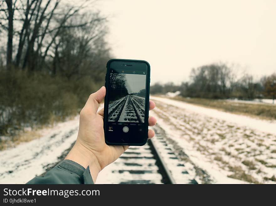 Person Holding Iphone Taking Photo of Train Rails