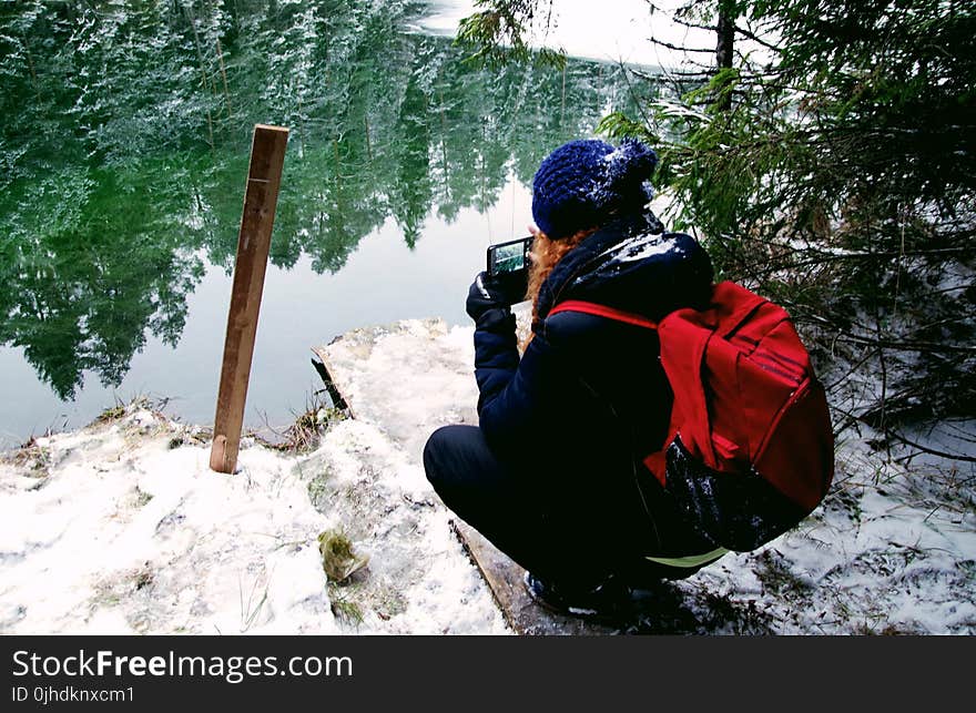 Person Carrying Red Backpack Capturing Photo Of Body Of Water