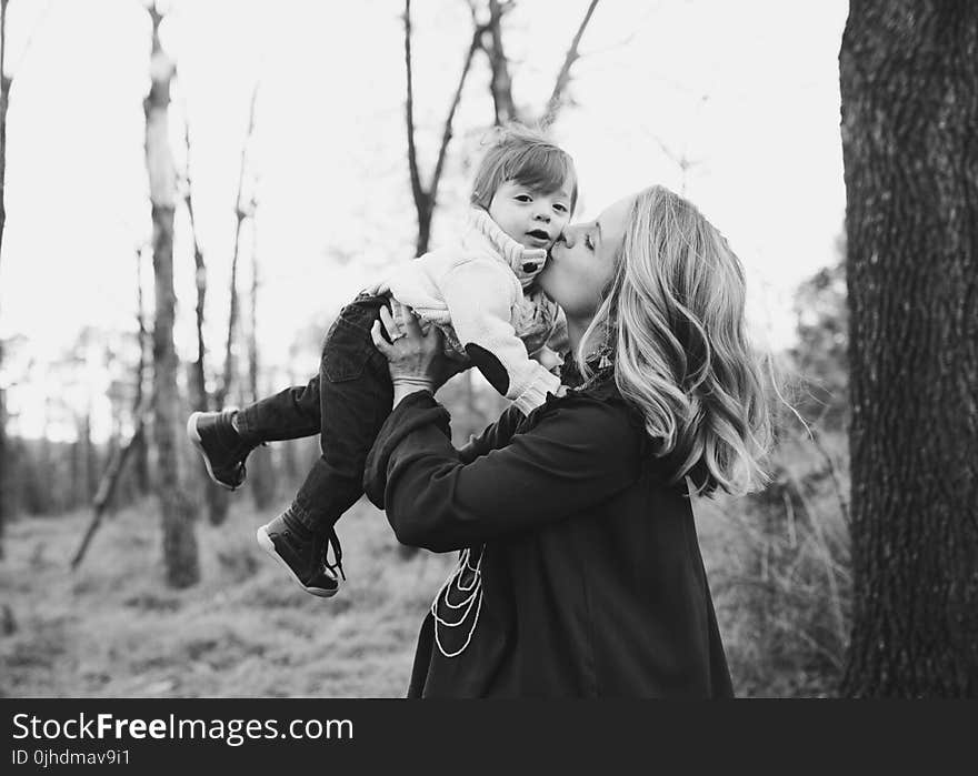 Grayscale Photo Of Woman Kissing Toddler On Cheek