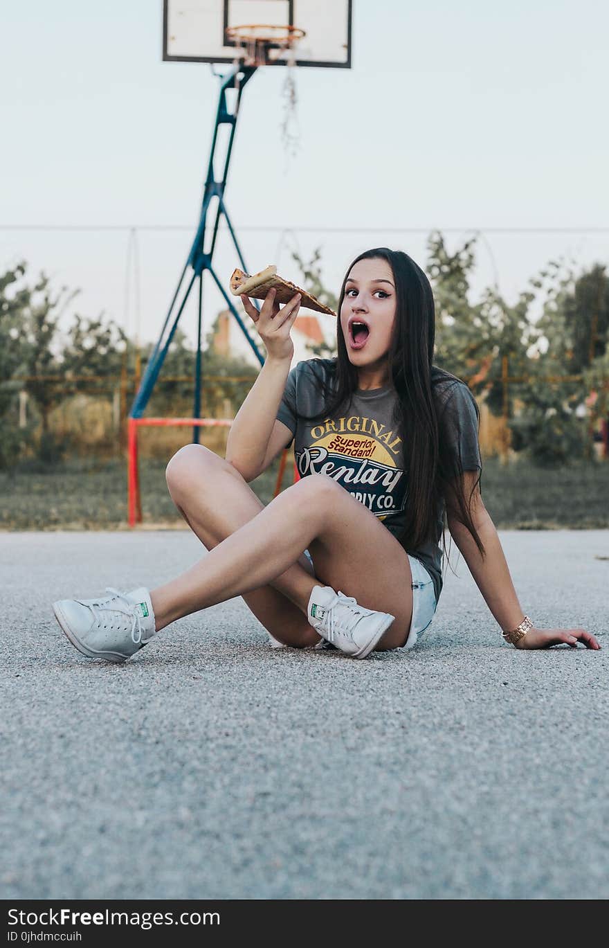 Girl Sitting on Basketball Field Holding Pizza