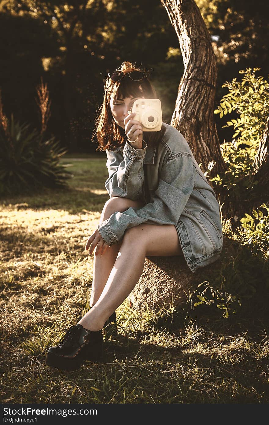 Woman Wearing Blue Denim Jacket Holding Pink Instant Camera Sitting on Soil