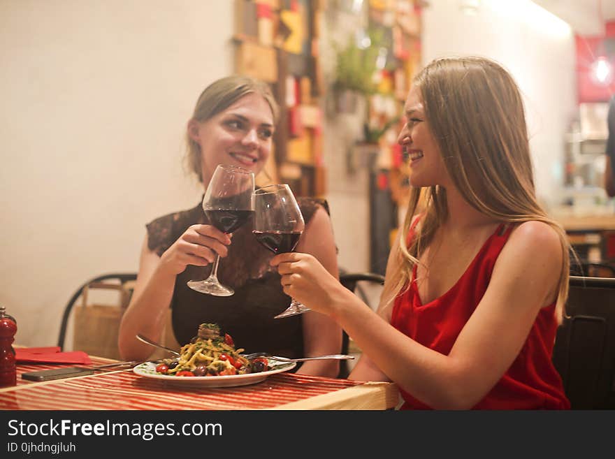 Two Women Holding Long-stem Wine Glasses With Red Liquid