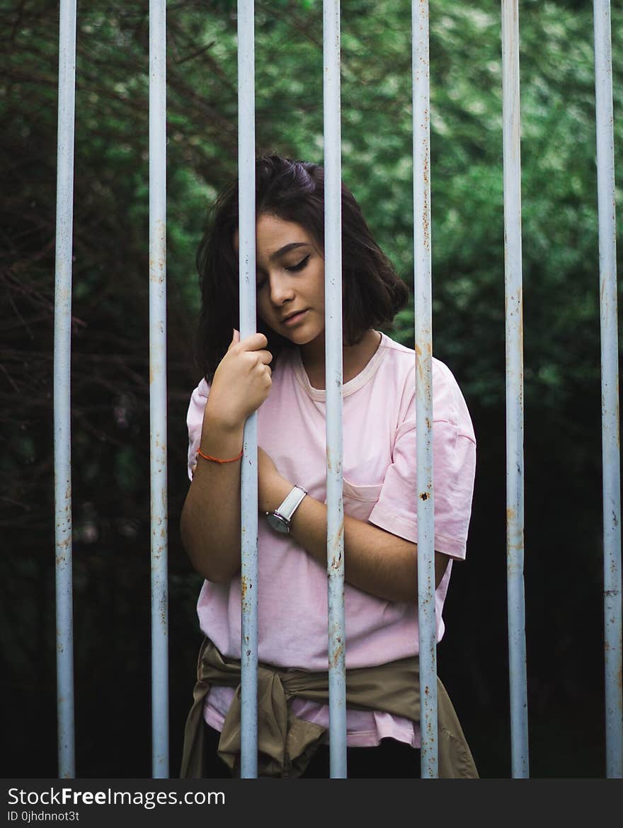 Woman Wearing Pink Crew-neck T-shirt Standing and Leaning Behind White Bars