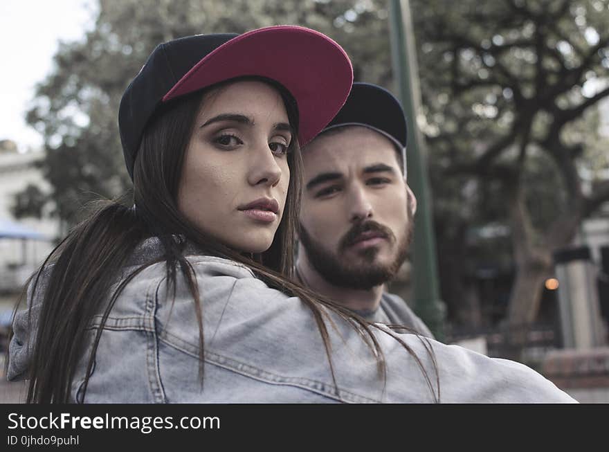 Woman in Blue Denim Jacket Near Man in Black Cap