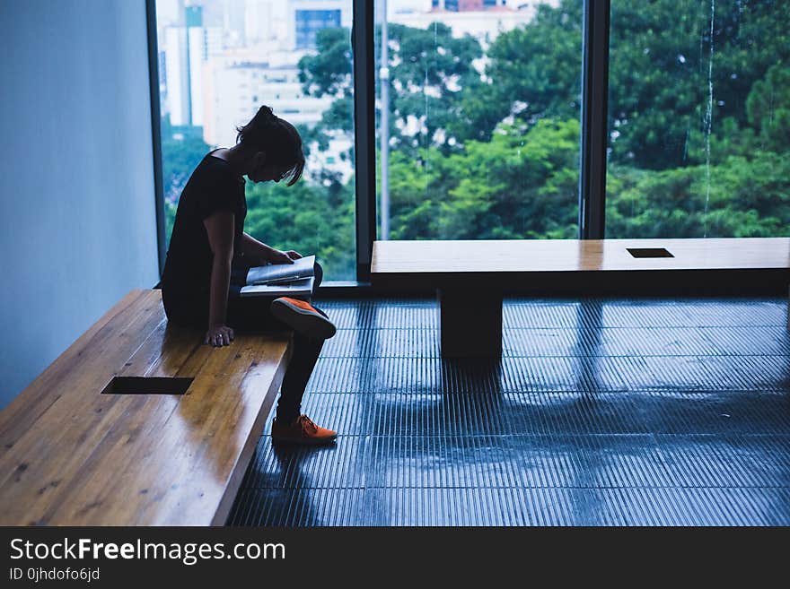 Woman Sitting On Brown Wooden Chair Beside Glass Window