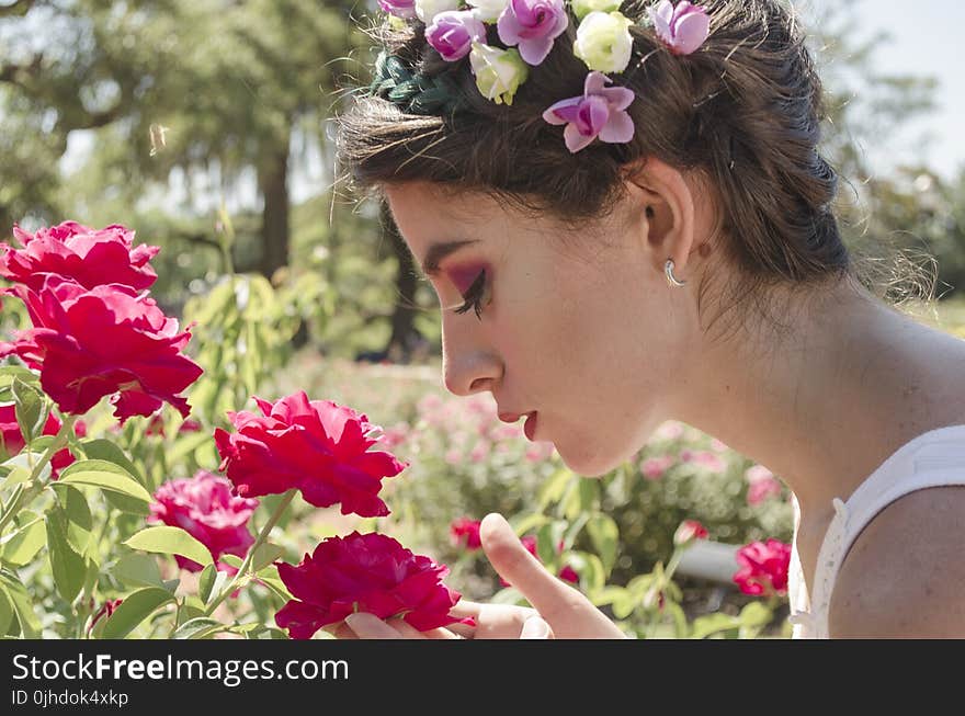 Woman in Floral Headdress Sniffing on Red Flowers