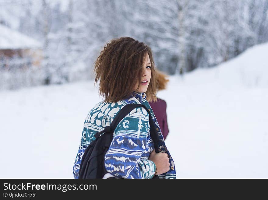 Selective Focus Portrait Photograph of Woman Wearing Blue, Green, and White Tribal Jacket and Black Backpack Outfit