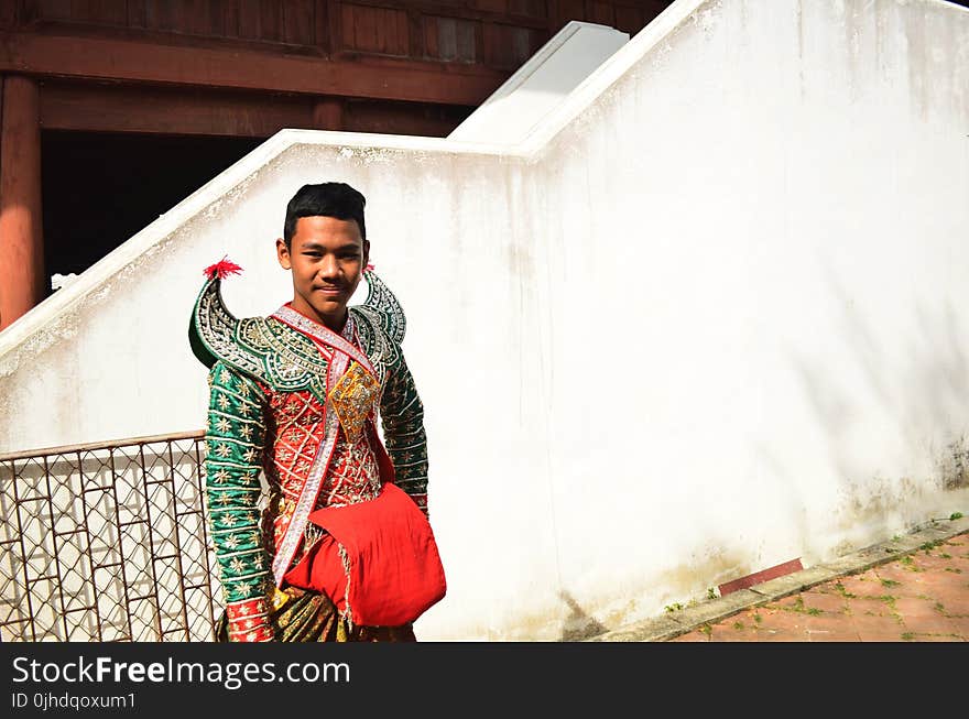 Man Wearing Green and Orange Costume Beside a Staircase