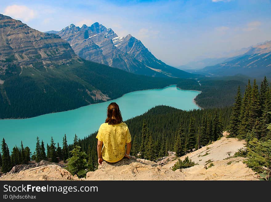 Person Sitting on Rocky Mountain Near Body of Water