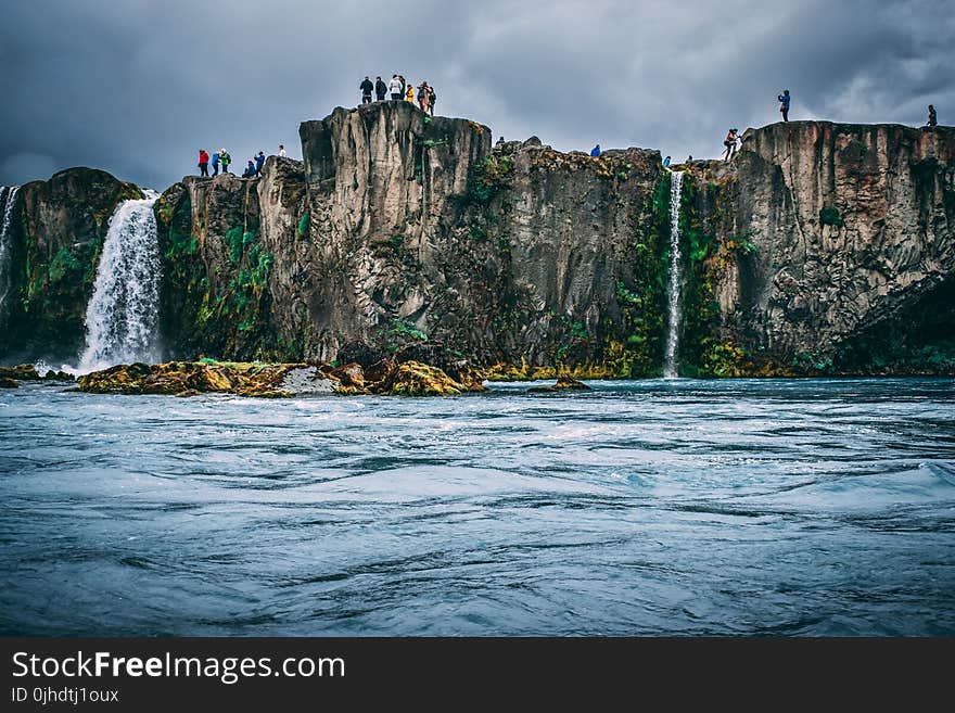 People Near Cliff Under Cloudy Sky