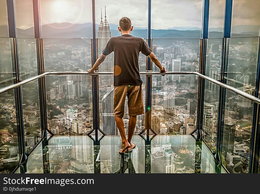 Man in Black T-shirt Looking Out of Glass Windows during Sunset